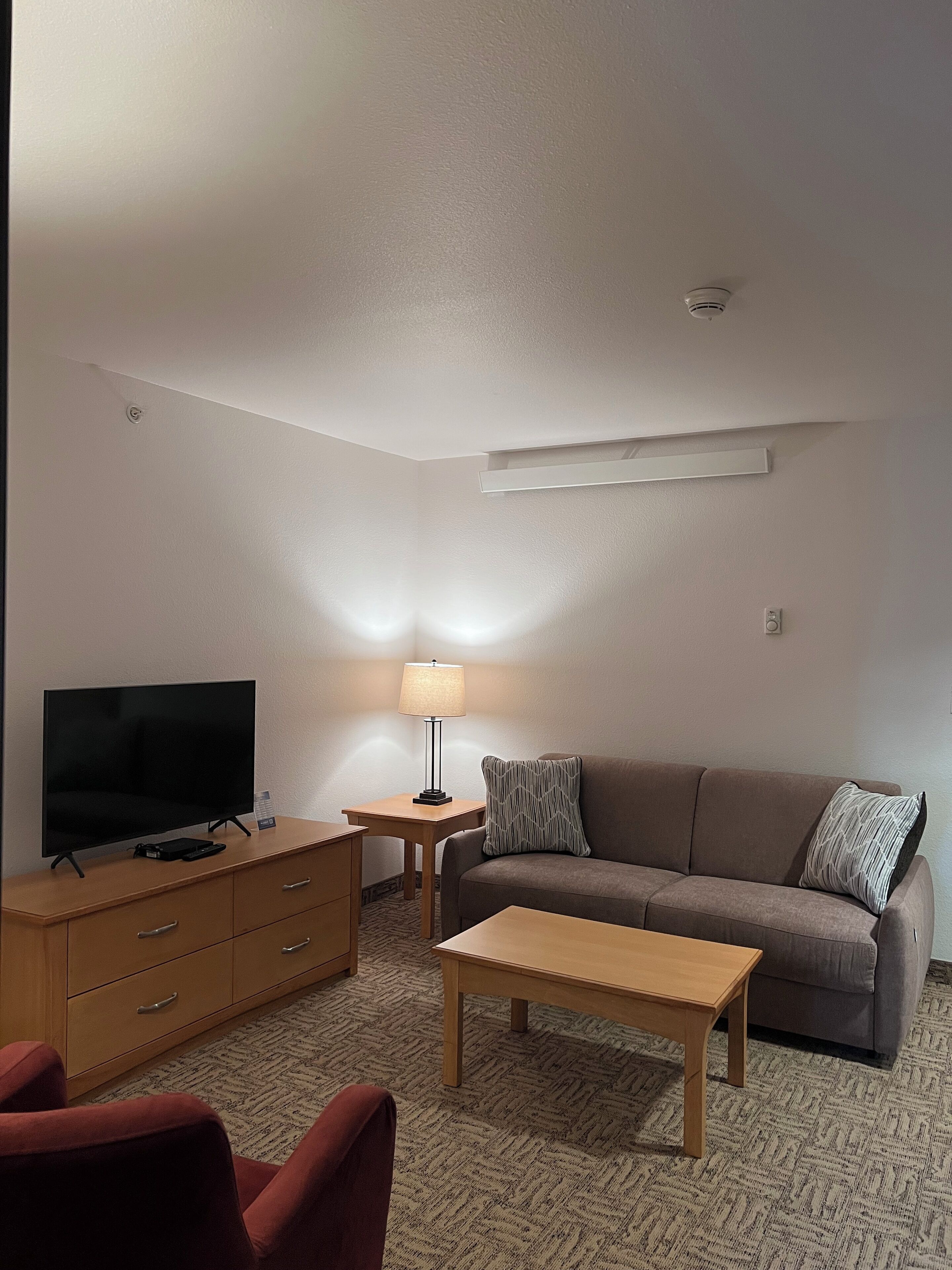 A living room with a flat-screen TV, a wooden coffee table, a sofa with patterned pillows, a lamp, and a small side table.