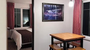 Et værelse med seng, et bord med stole, et billede i ramme på væggen og et vindue med gardiner.