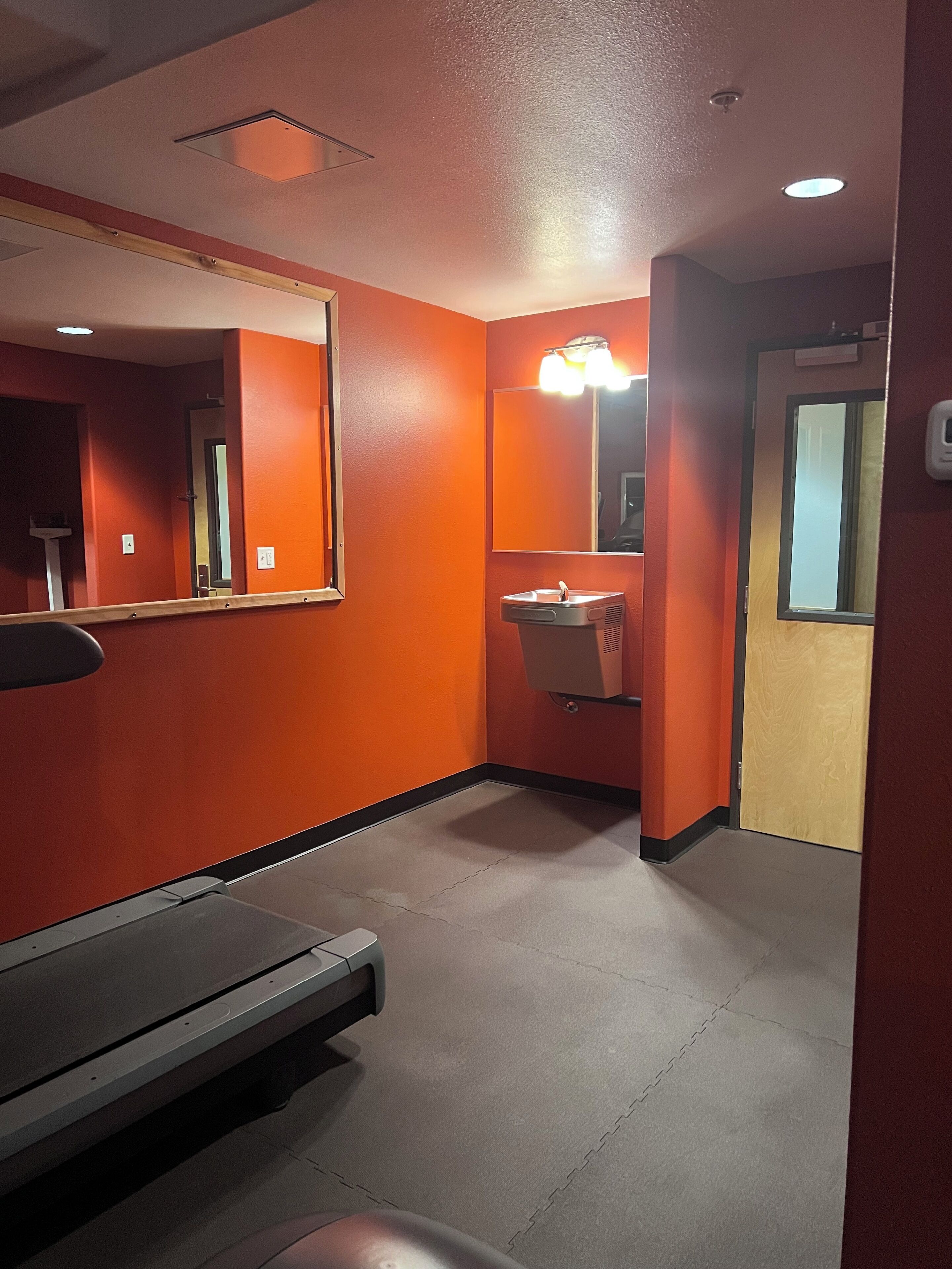 A restroom with orange walls, a mirror, a sink, and a bench.