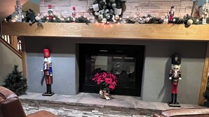 En pejs med en stenbeklædt kamin, to læderlænestole og et juletræ.