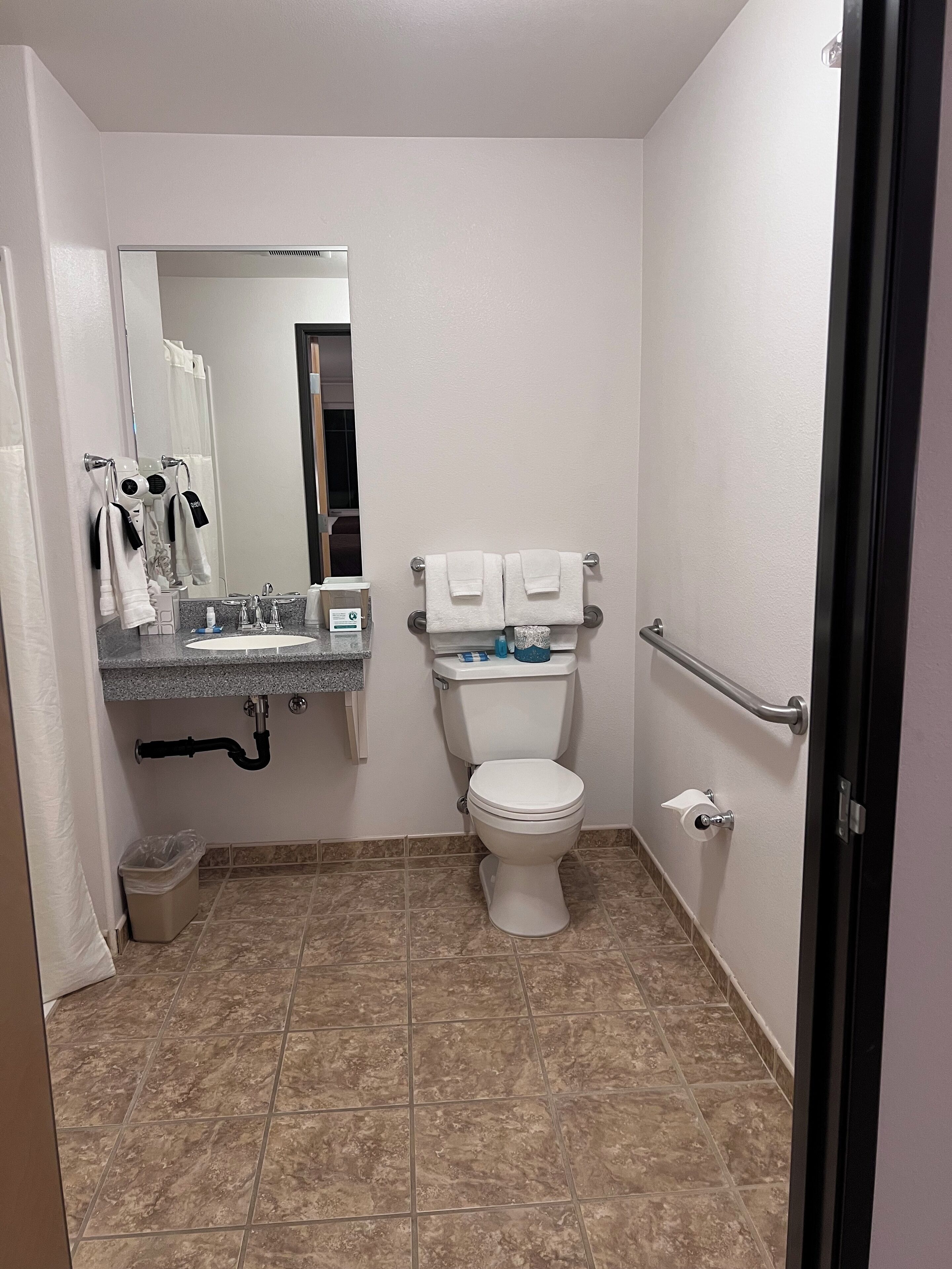 A small, clean bathroom with a toilet, sink, and mirror. There are towels and toiletries on the counter.