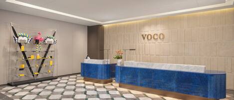 Ett receptionsområde med två blå receptionsdiskar, en väggmonterad skylt med texten ”VOCO” och ett mönstrat golv.