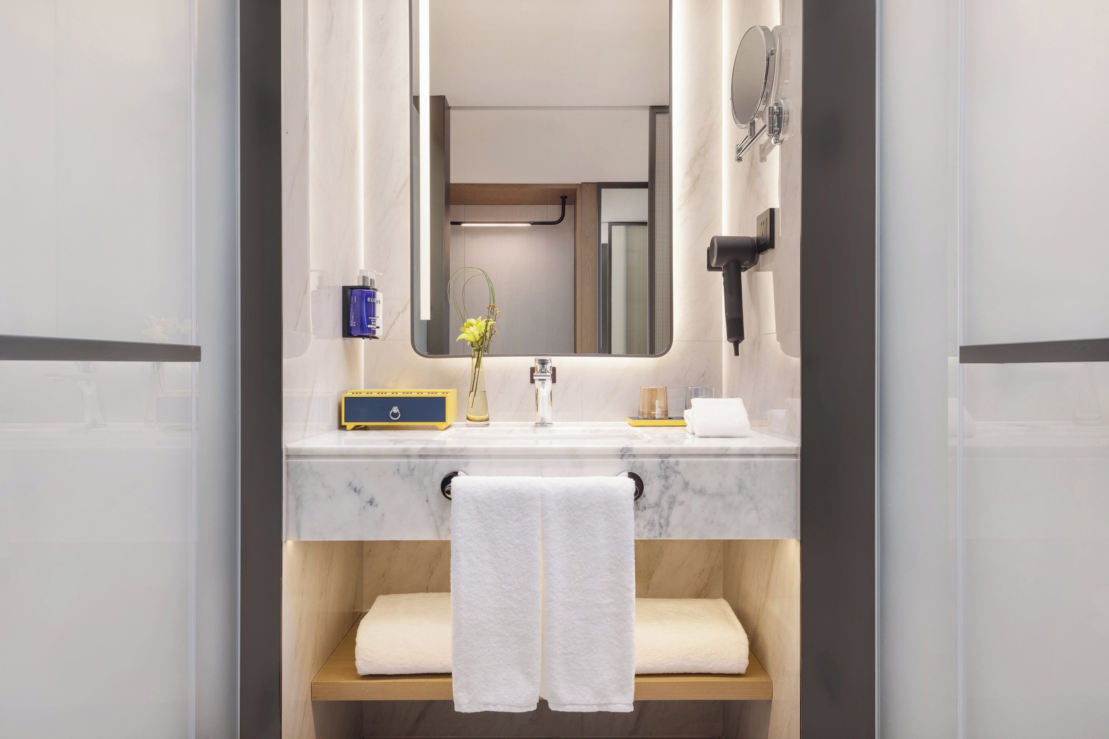 A bathroom with a marble sink, a mirror, a towel rack, and a wooden shelf.