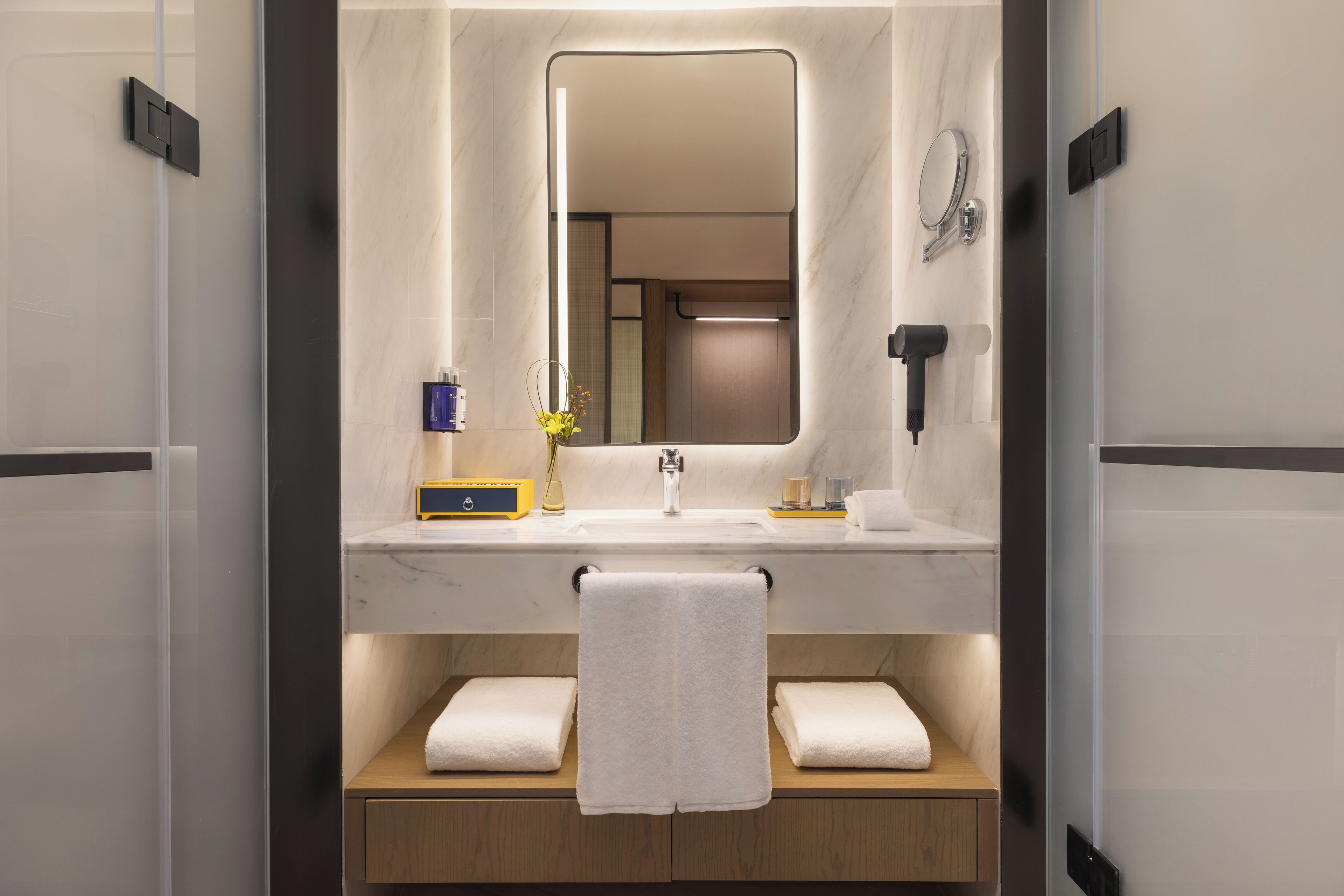 Un baño moderno con un espejo grande, un lavamanos y dos toallas sobre una repisa de madera.