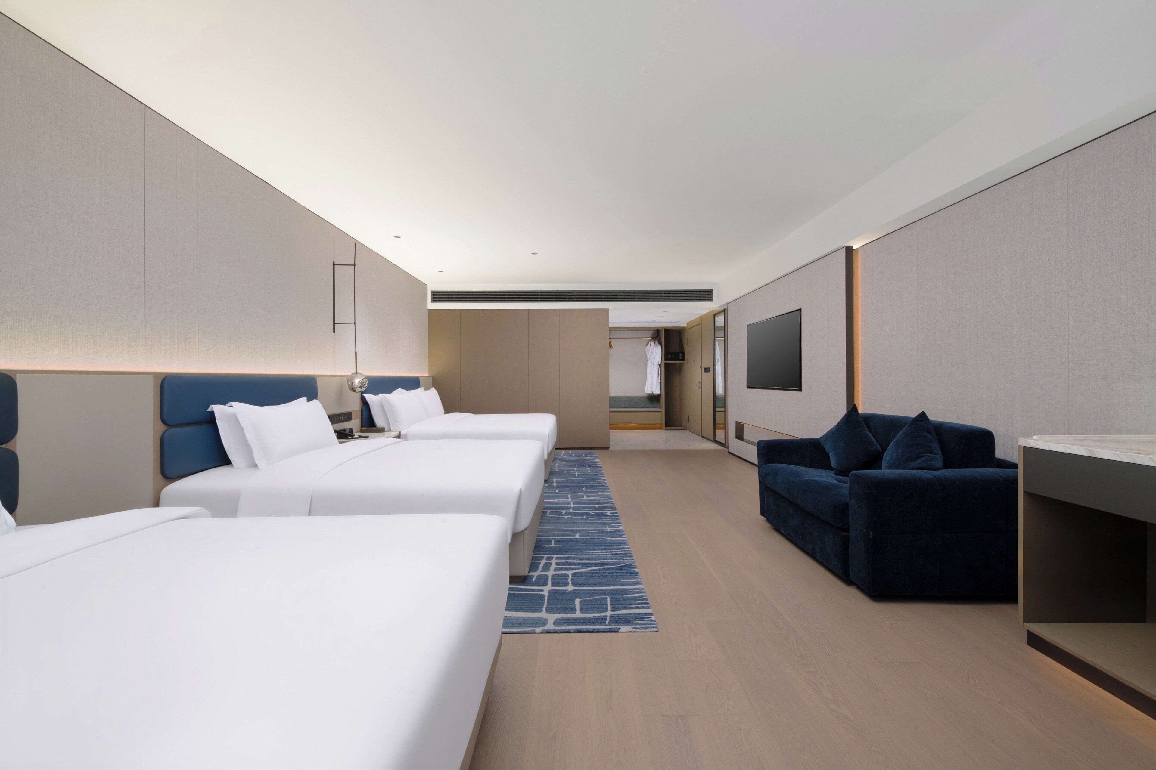 Habitación de hotel con tres camas, un sofá, una televisión y una kitchenette pequeña.