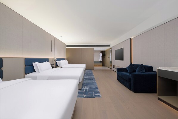 Ein Hotelzimmer mit drei Betten, einer Schlafcouch, einem Fernseher und einer kleinen Küchenzeile.
