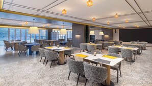 Une salle de conférence équipée de tables et de chaises, de grandes fenêtres et de luminaires au plafond.