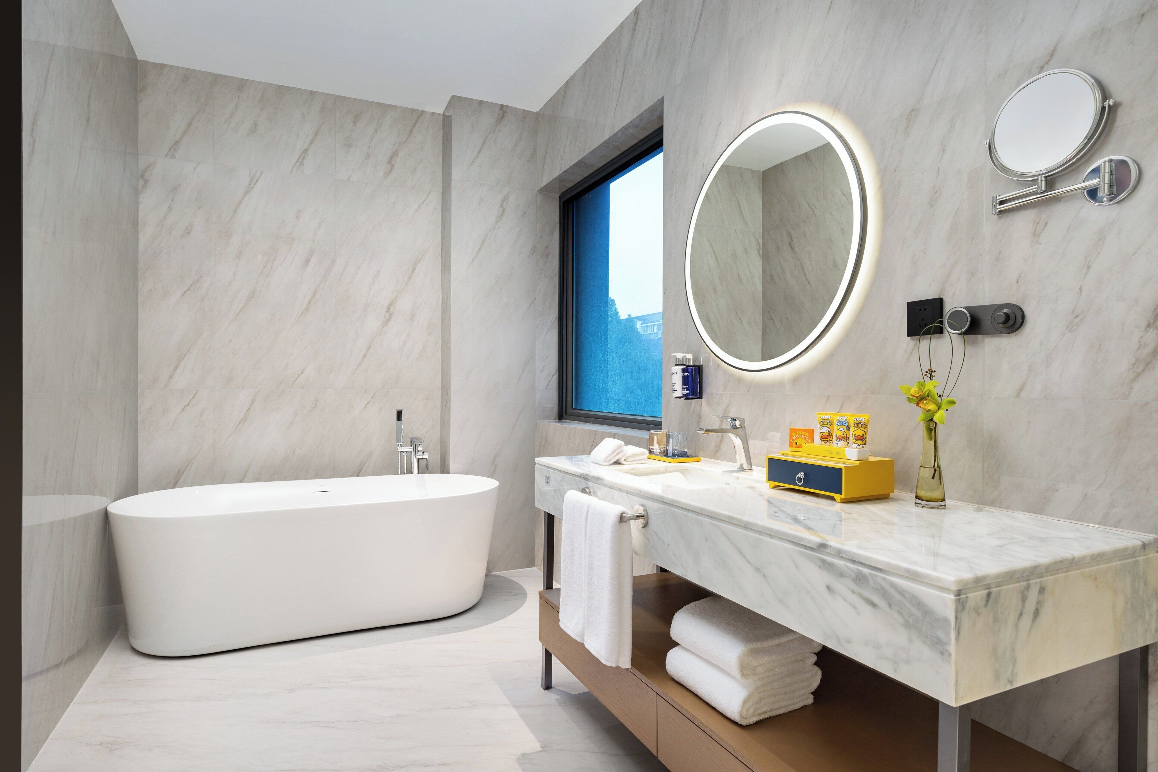 A modern bathroom with a freestanding bathtub, a marble vanity, a large mirror, and a window.