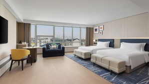 Une chambre d  ’hôtel moderne équipée de deux lits, d’un canapé, d’un bureau et d’une grande fenêtre donnant sur la ville.