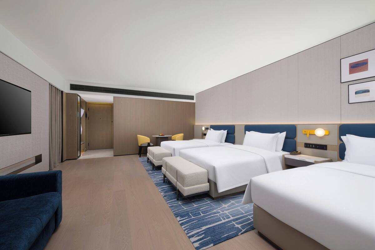 A hotel room with a large bed, two smaller beds, a TV, a desk, and a chair.
