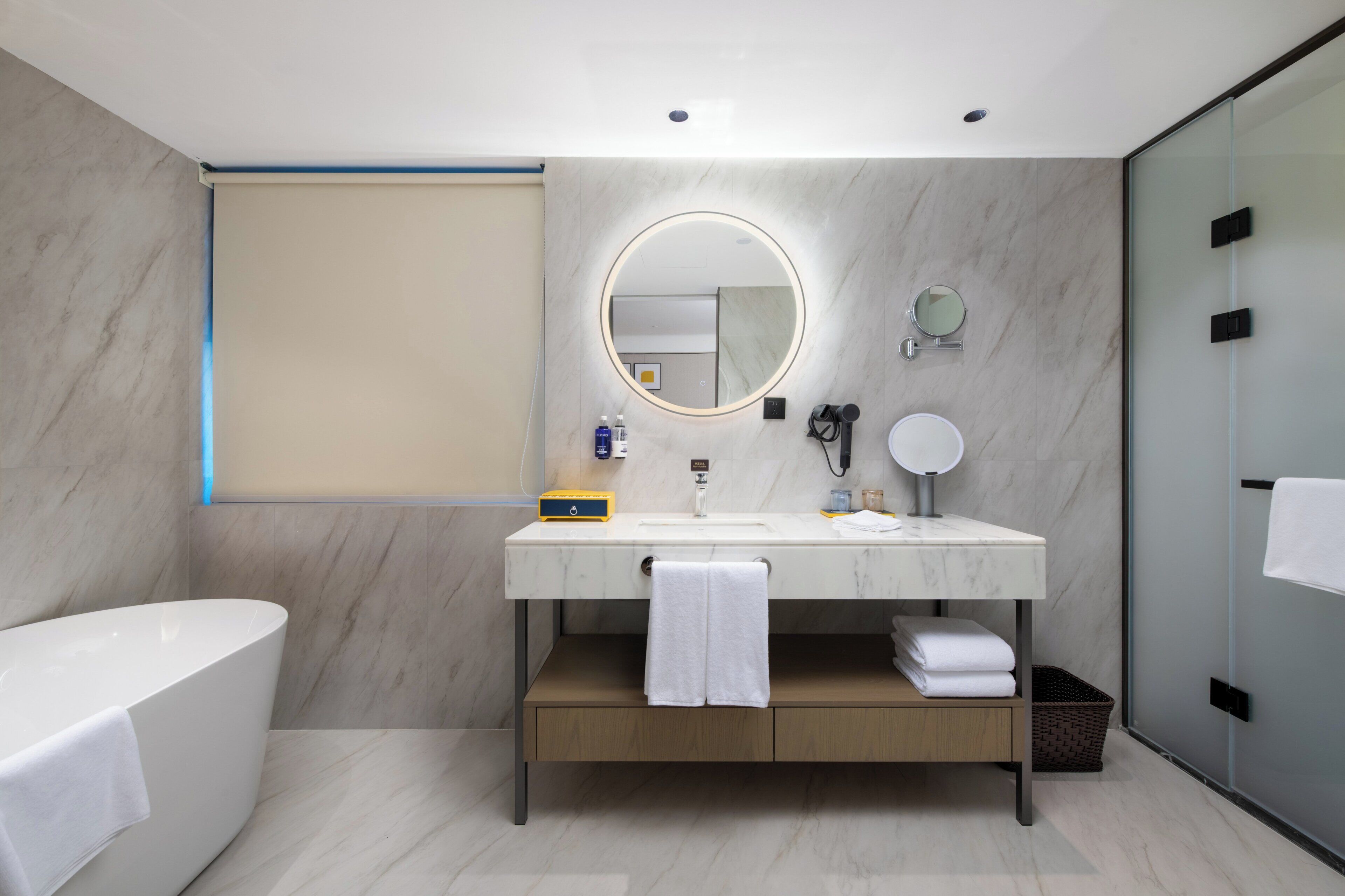 A modern bathroom with a marble vanity, a round mirror, a bathtub, and a glass shower enclosure.