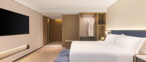 A modern hotel room with a large bed, a flat-screen TV mounted on the wall, a walk-in closet, and a bathroom with a robe hanging on a rack.