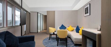 A modern hotel room with a sofa, chairs, a small table, a fireplace, and large windows.