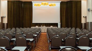 A conference room with rows of chairs facing a projection screen, a table with a white tablecloth, and a carpeted floor.