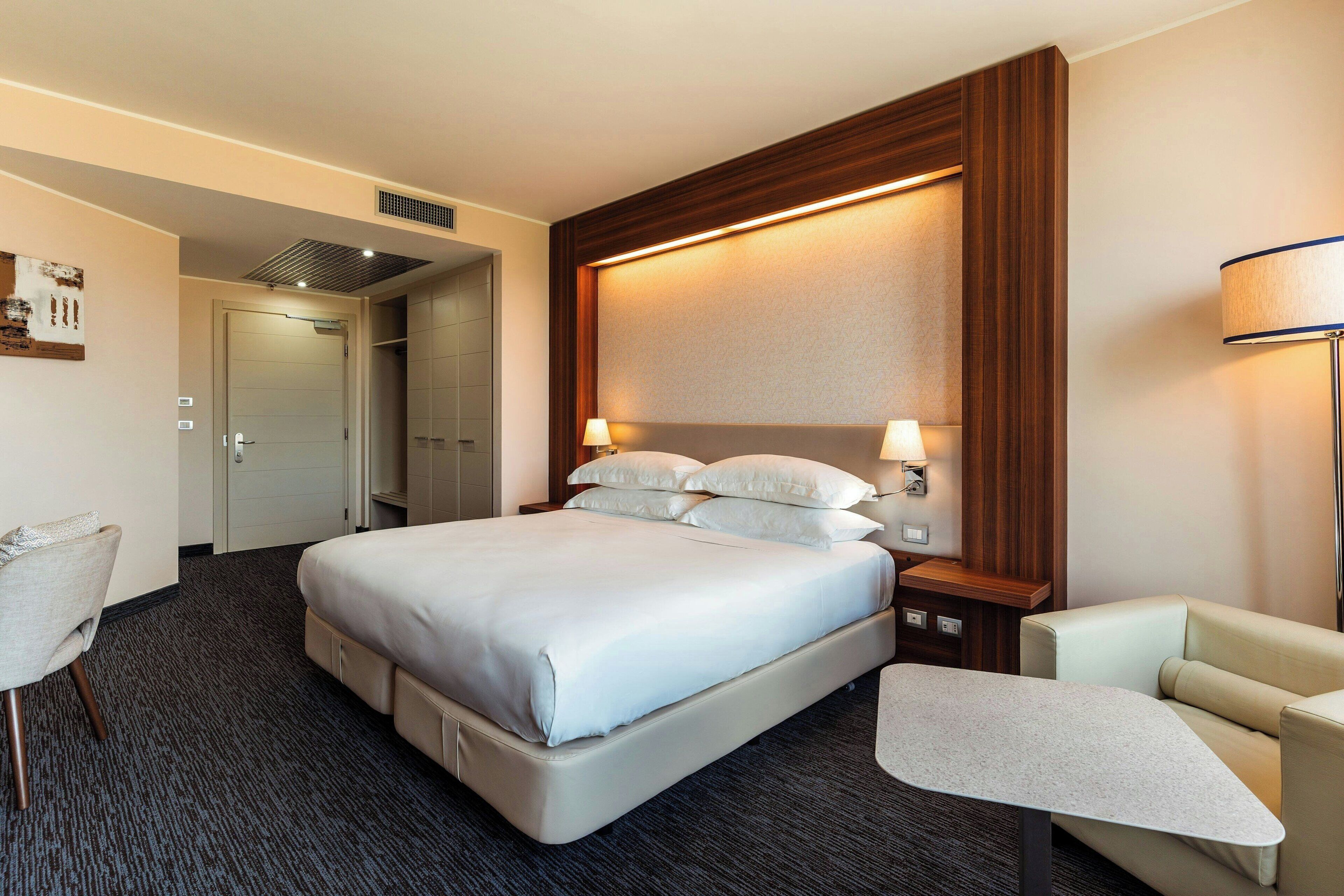 Habitación de hotel con una cama grande, un escritorio, una silla y un armario.