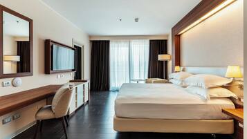 Habitación de hotel con una cama grande, un escritorio con una silla, un televisor y una ventana con cortinas.