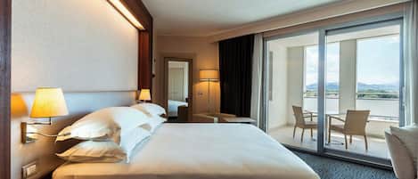 Habitación de hotel con una cama grande, un escritorio, una silla y un balcón con mesa y sillas.