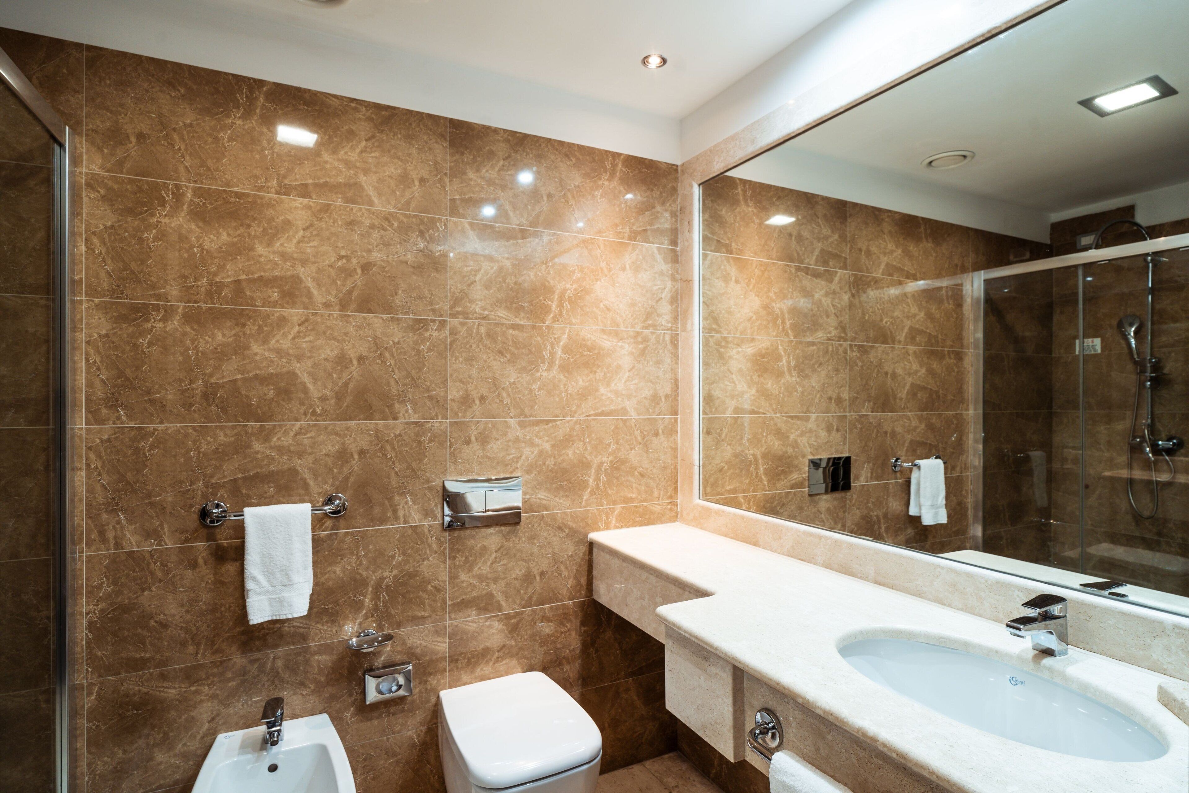 Ein modernes Badezimmer mit Marmorwand, Waschbecken, Toilette und Duschbereich.