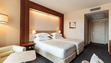 Une chambre d’hôtel avec deux lits, une petite table, un canapé et une porte donnant sur une salle de bain.