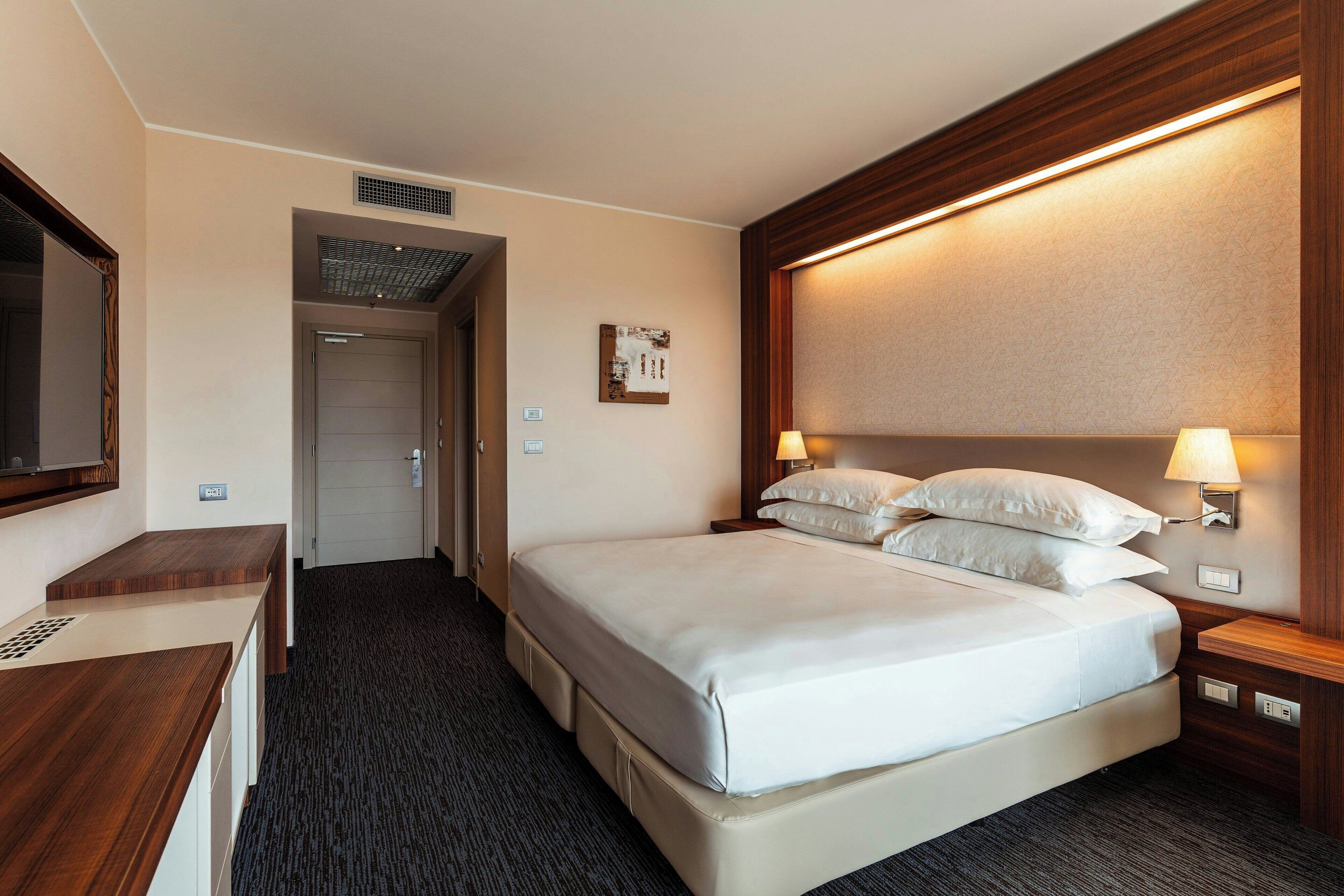 Una habitación de hotel con una cama grande, un escritorio y un espejo.