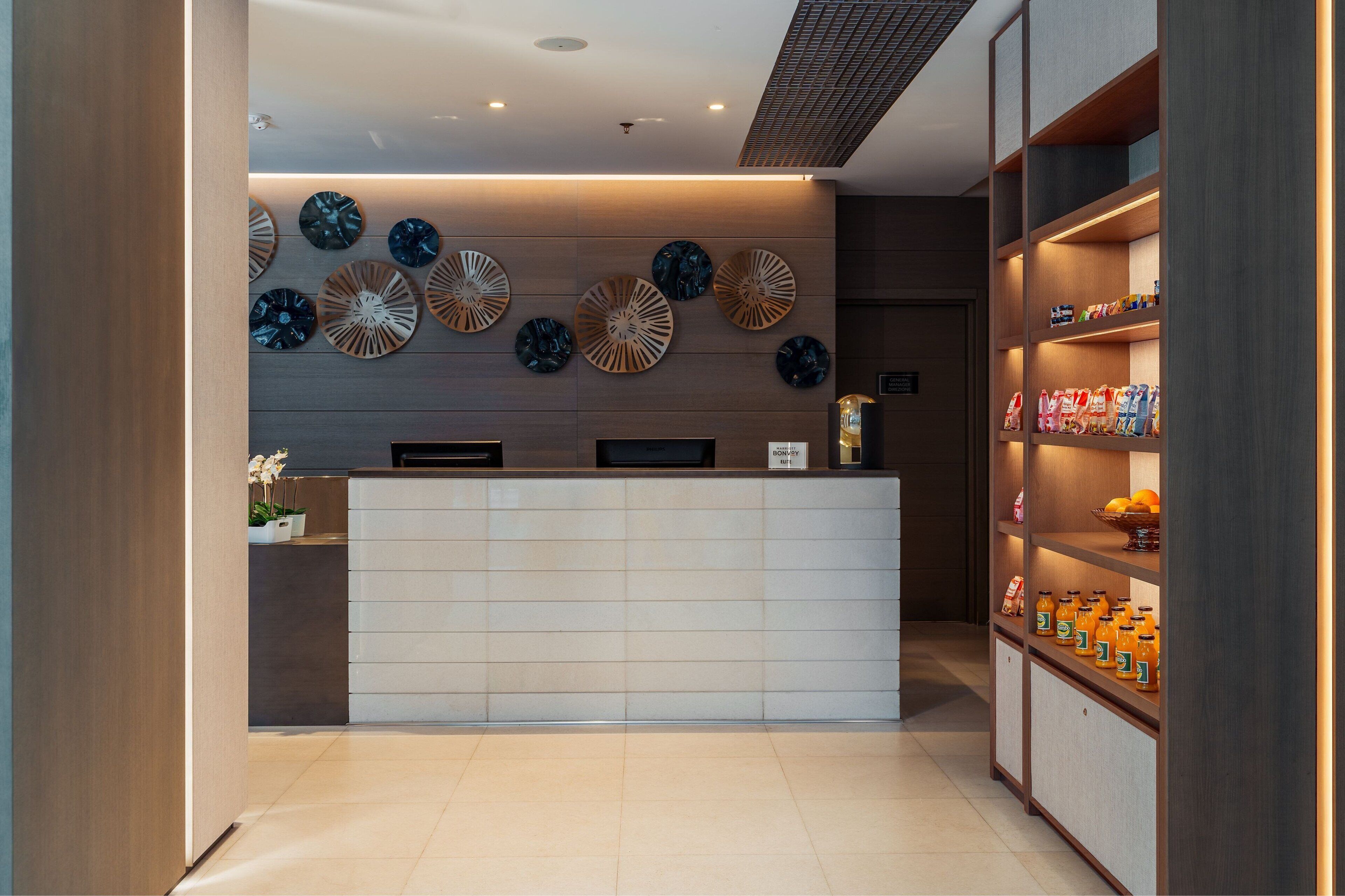 A reception area with a modern design, featuring a reception desk, decorative wall art, and a shelf with bottled water.