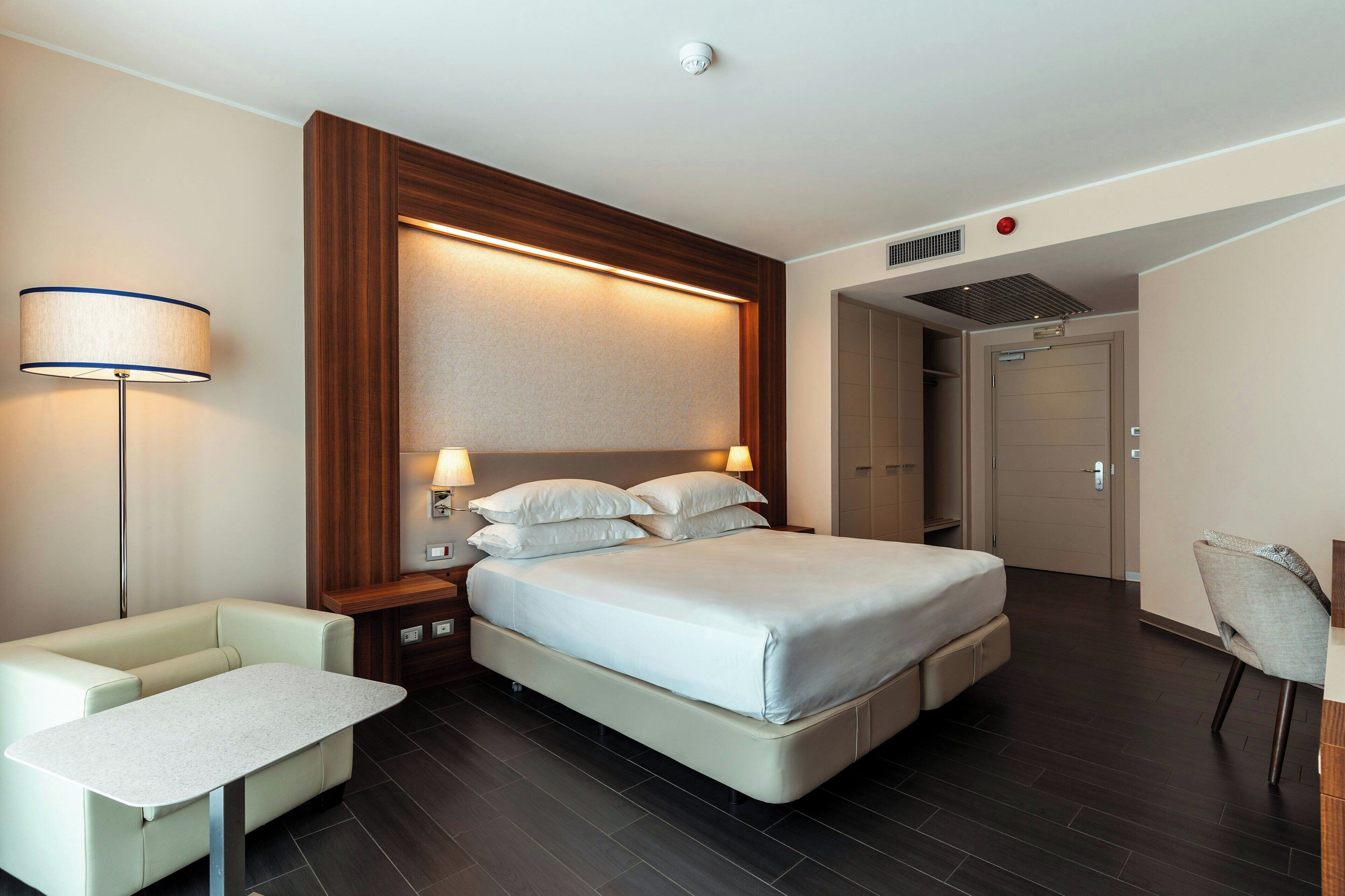 A modern hotel room with a large bed, bedside tables, a desk, and a chair.