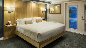 A hotel room with a large bed, wooden headboard, two bedside tables with lamps, a mirror, and a door leading to a balcony.