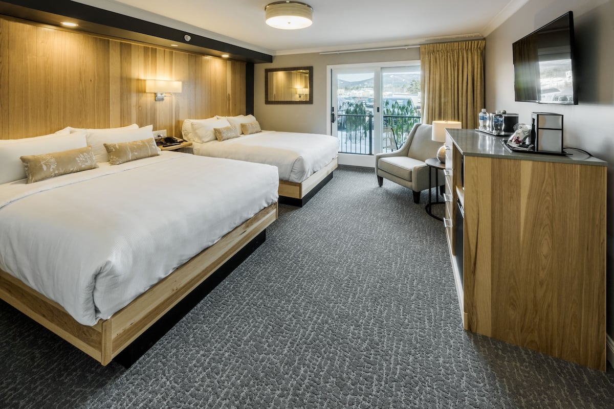 A hotel room with two beds, a desk, a chair, a TV, and a balcony with a view.