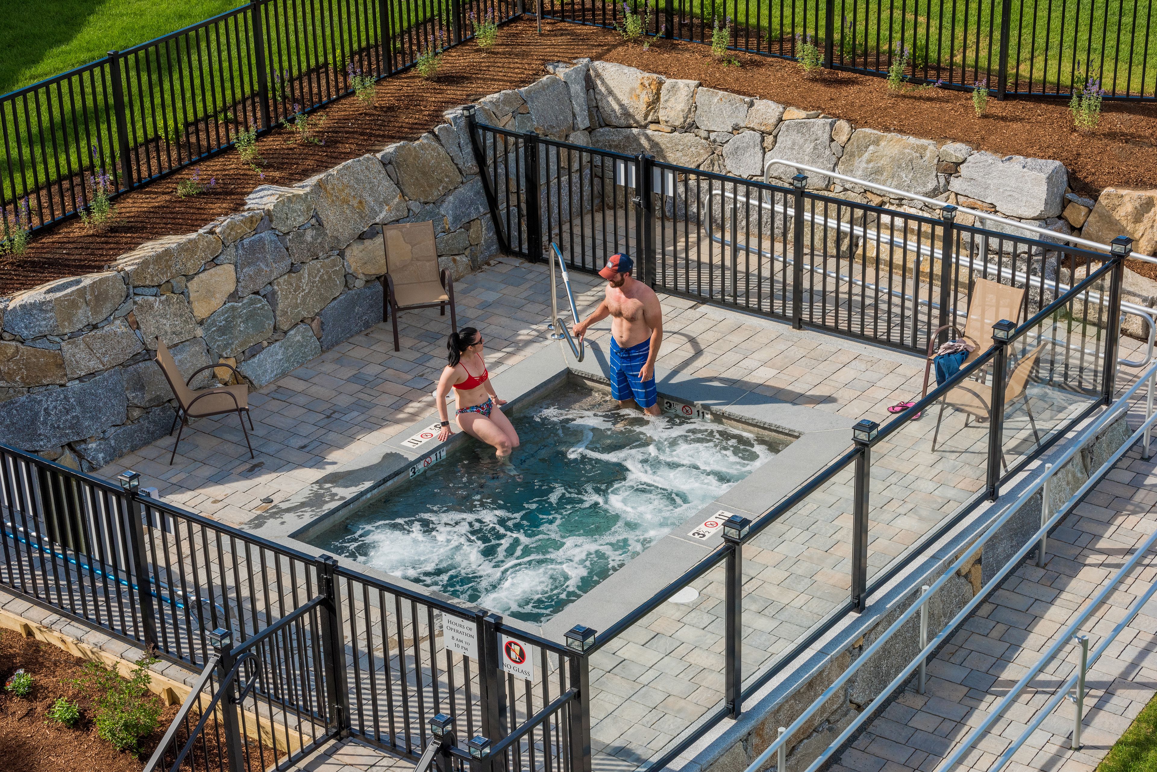 A swimming pool with stone walls and metal railings, surrounded by a paved deck and a stone border.