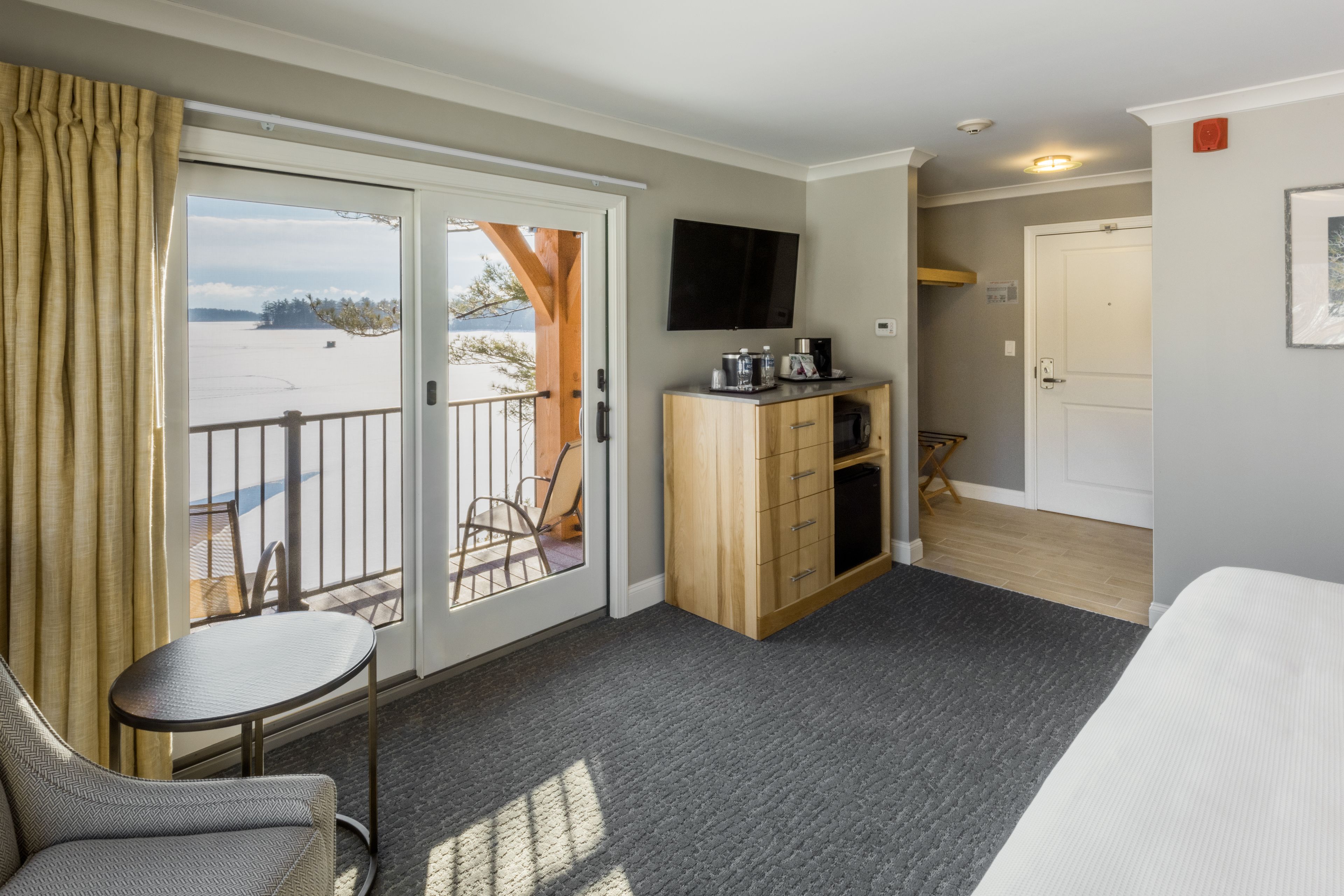 Une chambre d’hôtel avec un balcon, une petite table, un canapé, une télévision et une armoire en bois.