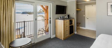 A hotel room with a balcony, a small table, a sofa, a TV, and a wooden cabinet.