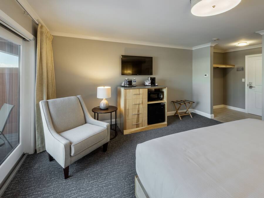 Una habitación de hotel con cama, una silla, un escritorio con lámpara, televisión y armario.