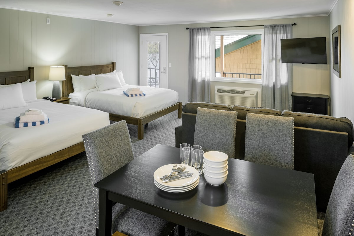 A hotel room with two beds, a dining table with plates and cutlery, a TV, and a window with curtains.
