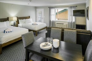 A hotel room with two beds, a dining table with plates and cutlery, a TV, and a window with curtains.