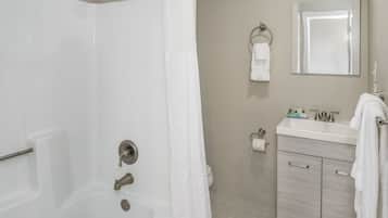 Een badkamer met een bad, douche, toilet, wastafel en spiegel.