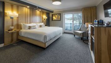 Quarto de hotel com uma cama grande, uma escrivaninha, uma cadeira e uma varanda com vista.
