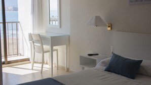 A hotel room with a bed, a desk, a chair, a nightstand, and a view of the beach. - Sicania (Cullera)