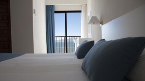 A hotel room with a large bed, a view of the sea through a balcony, and a lamp on the wall. - Sicania (Cullera)