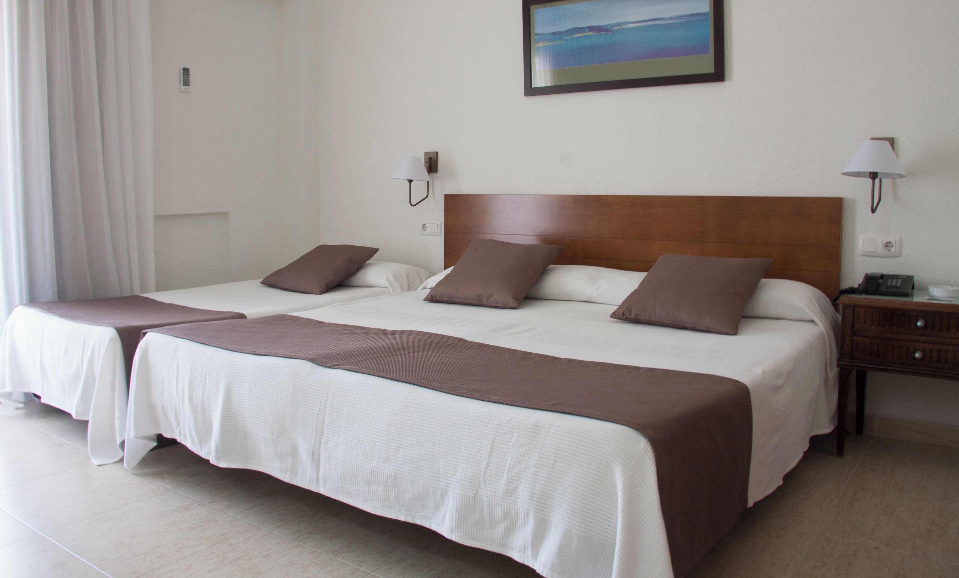 A hotel room with two beds, a headboard, bedside lamps, a painting on the wall, and a telephone on the nightstand.