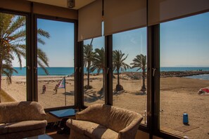 A room with large windows overlooking a beach, featuring palm trees and a clear view of the sea. - Sicania (Cullera)