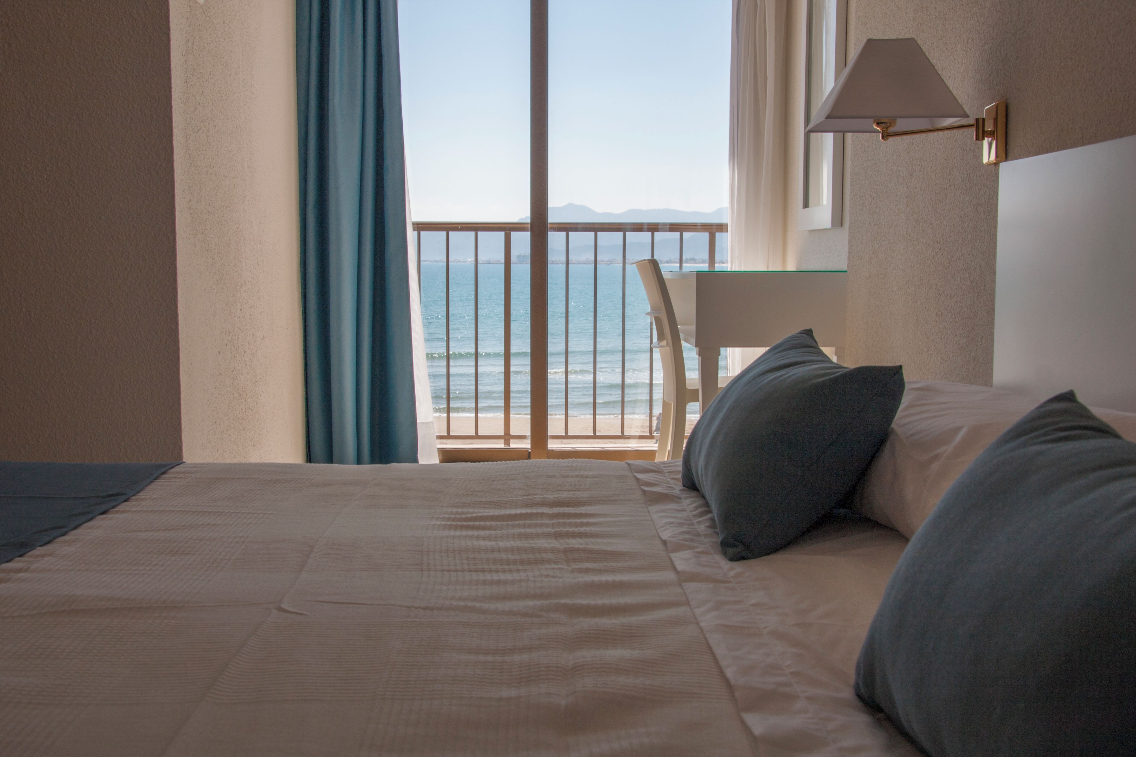 A hotel room with a bed, a chair, a view of the sea, and a balcony with a railing.