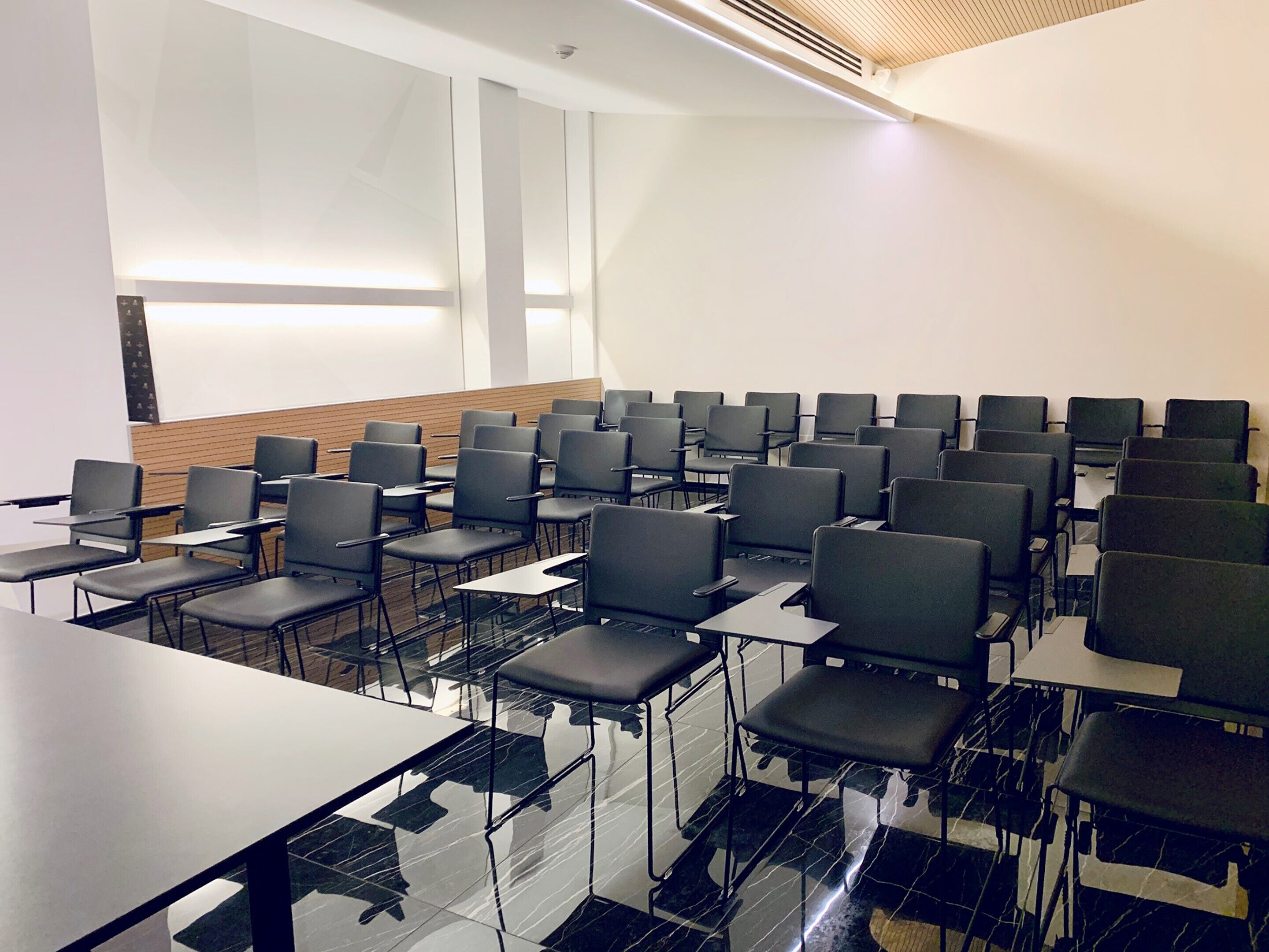 Ein Konferenzraum mit Reihen von Stühlen und Tischen, einer Holzwand und einer großen Whiteboard-Tafel.