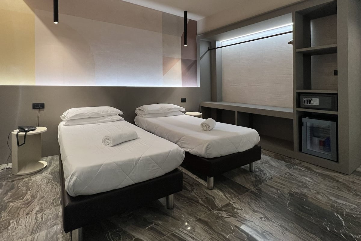 Quarto de hotel com duas camas, um minibar, uma mesinha e uma televisão montada na parede.