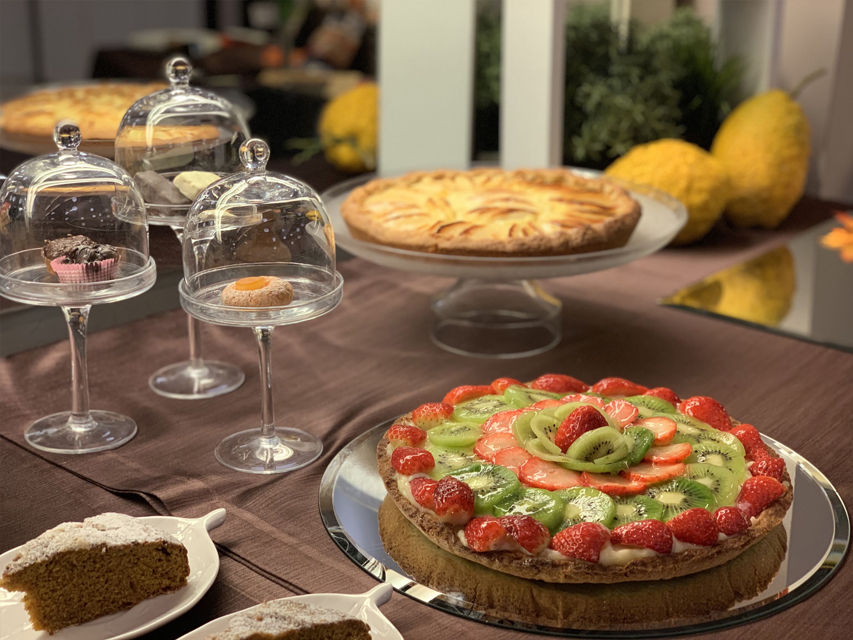 Un tavolo con dolci assortiti, tra cui una crostata di frutta e una fetta di torta su un piatto.