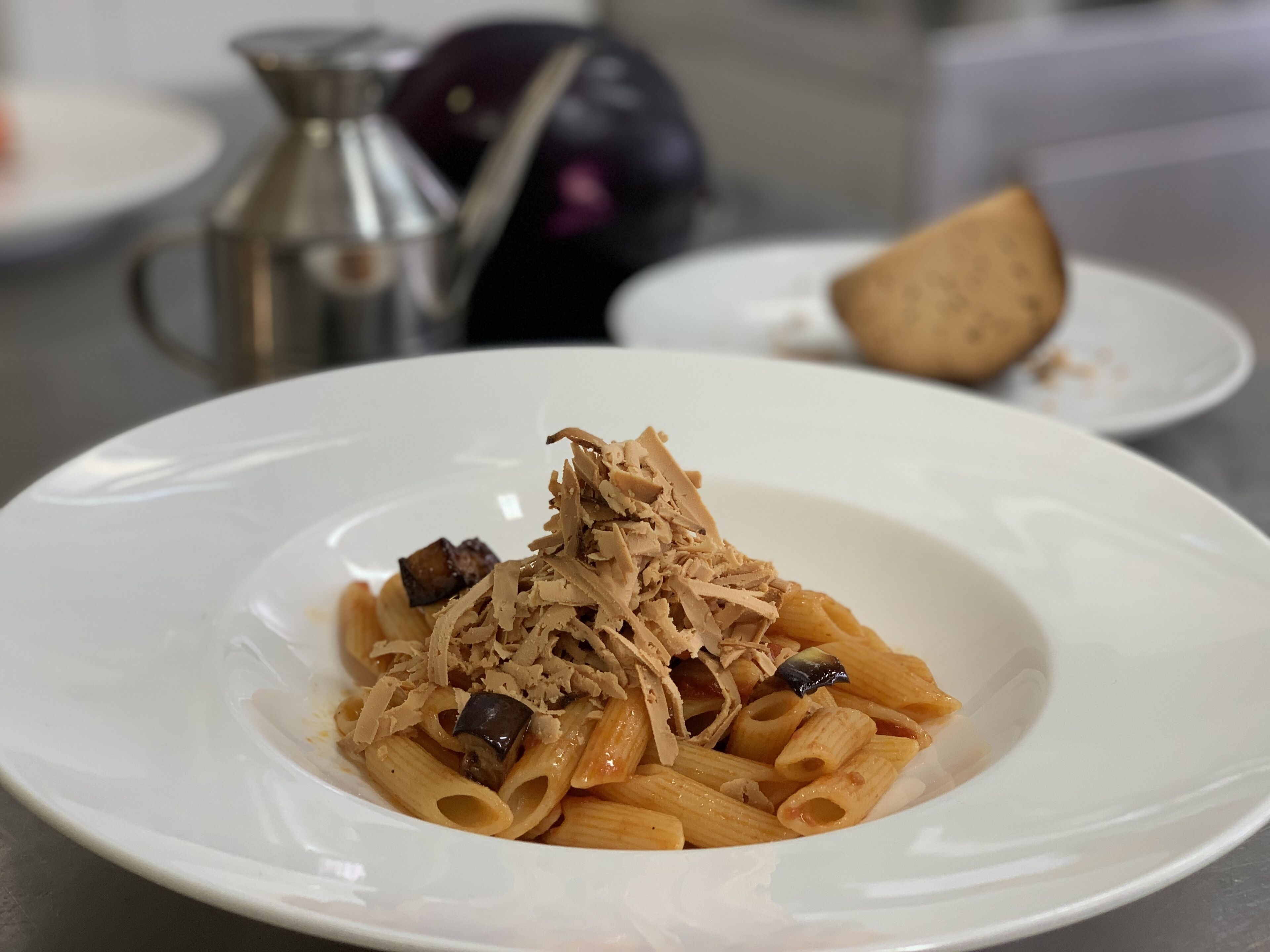 Een witte schaal pasta, belegd met geraspte kaas en een stukje paddenstoel.