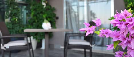 An outdoor patio area with a table and chairs, surrounded by lush greenery and flowering plants.