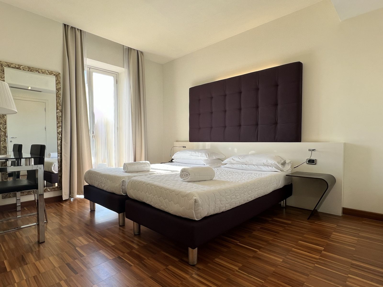 Cama doble con cabecera oscura, dos mesitas de noche y un espejo sobre la cama.