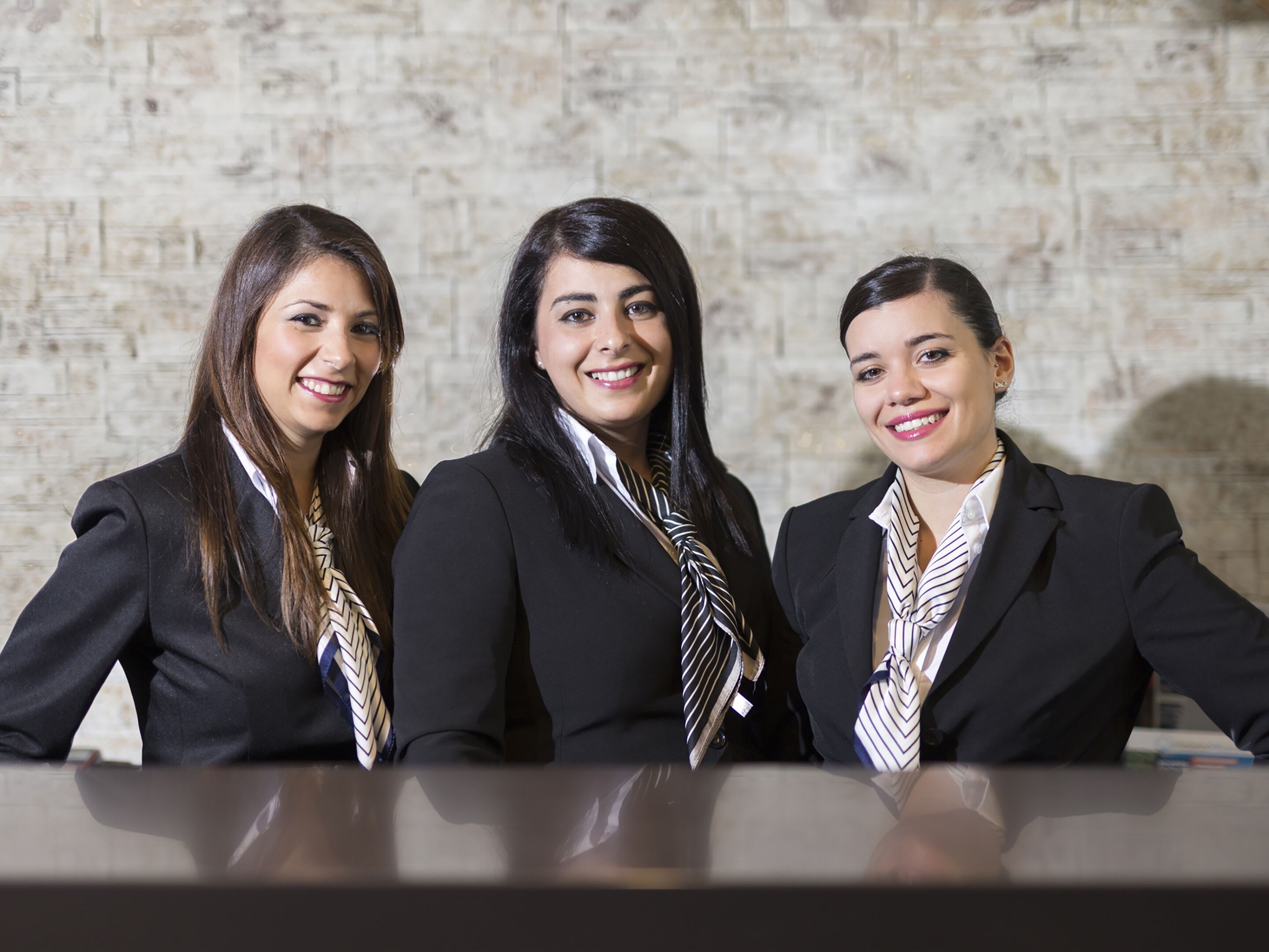 Tres personas vestidas con traje sentadas a una mesa con un muro de piedra de fondo.