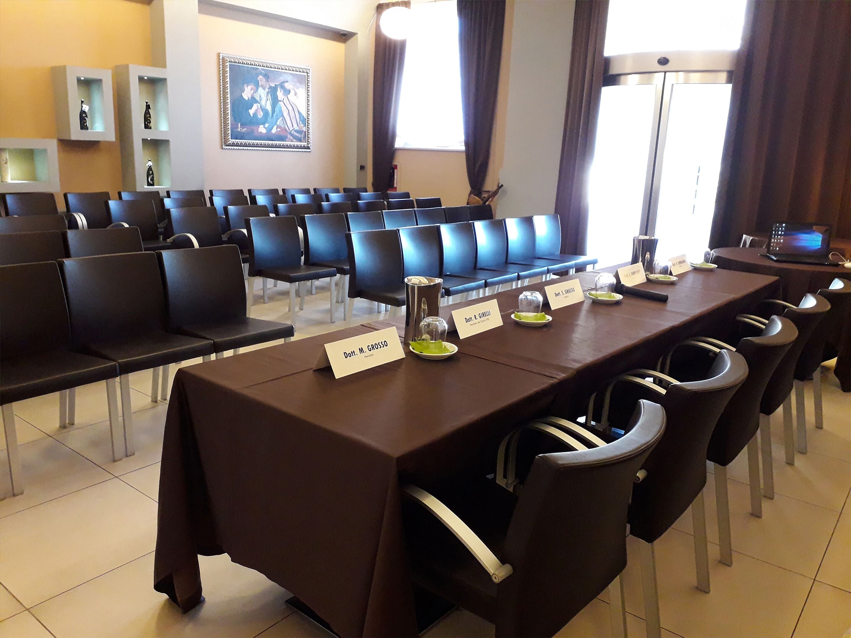A conference room with rows of chairs, a long table with nameplates, and a painting on the wall.
