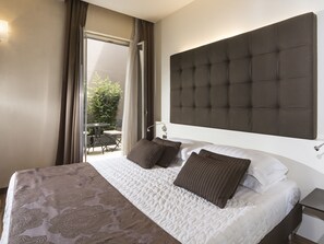 A hotel room with a large bed, a headboard, a bedside table, and a view of an outdoor patio. - Hotel La Bussola (Milazzo)